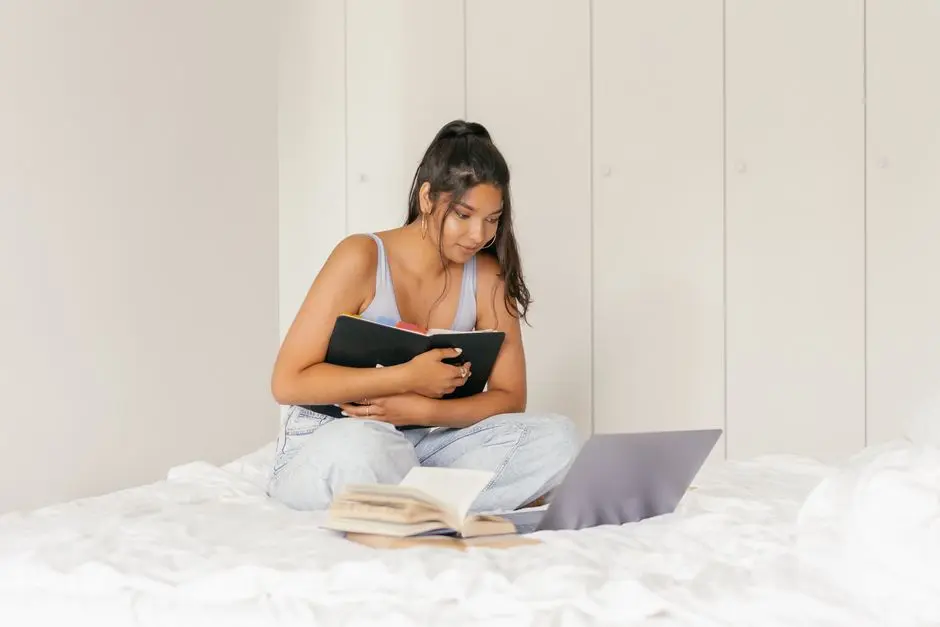 Seorang mahasiswa belajar dengan laptop di kamar, dikelilingi buku dan catatan